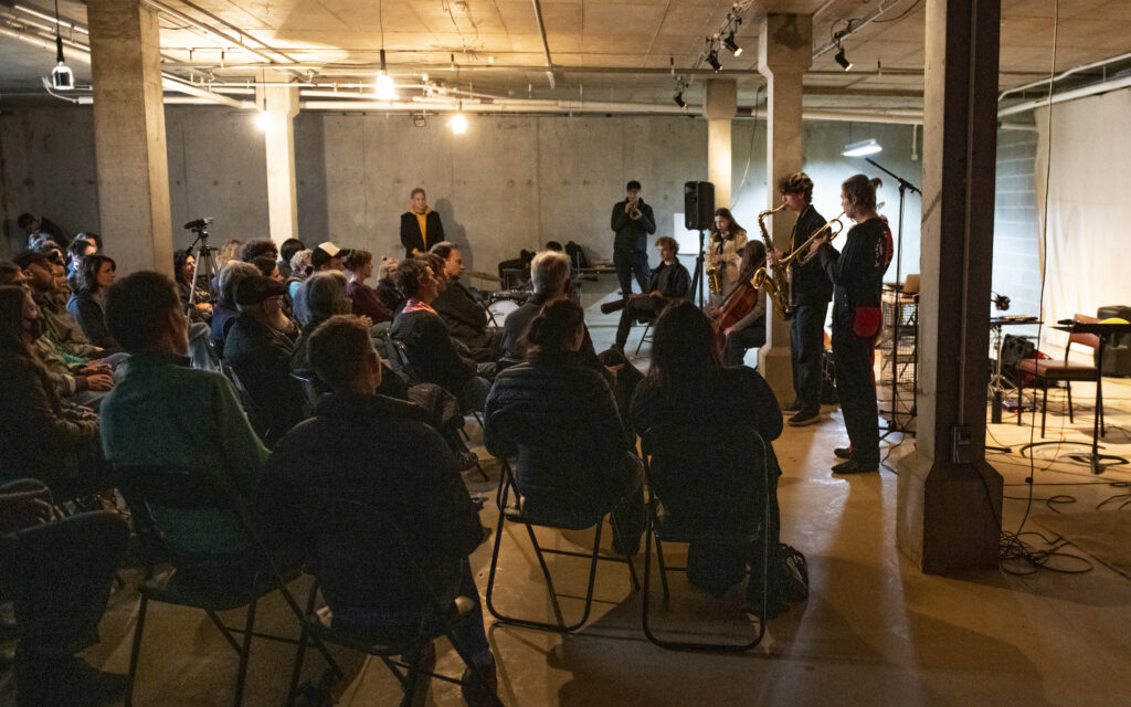 A group of sonic artists performing to a crowd of seated audience in a Punctum's ICU underground space.